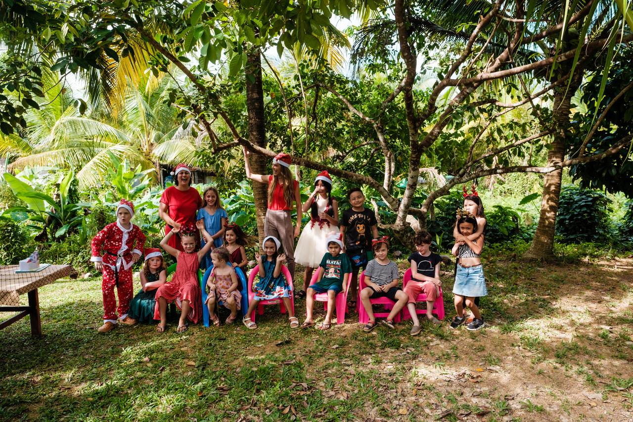 Grupa dzieci z klasy w Tajlandii, na Koh Lancie. Stoją wśród egzotycznych drzew.