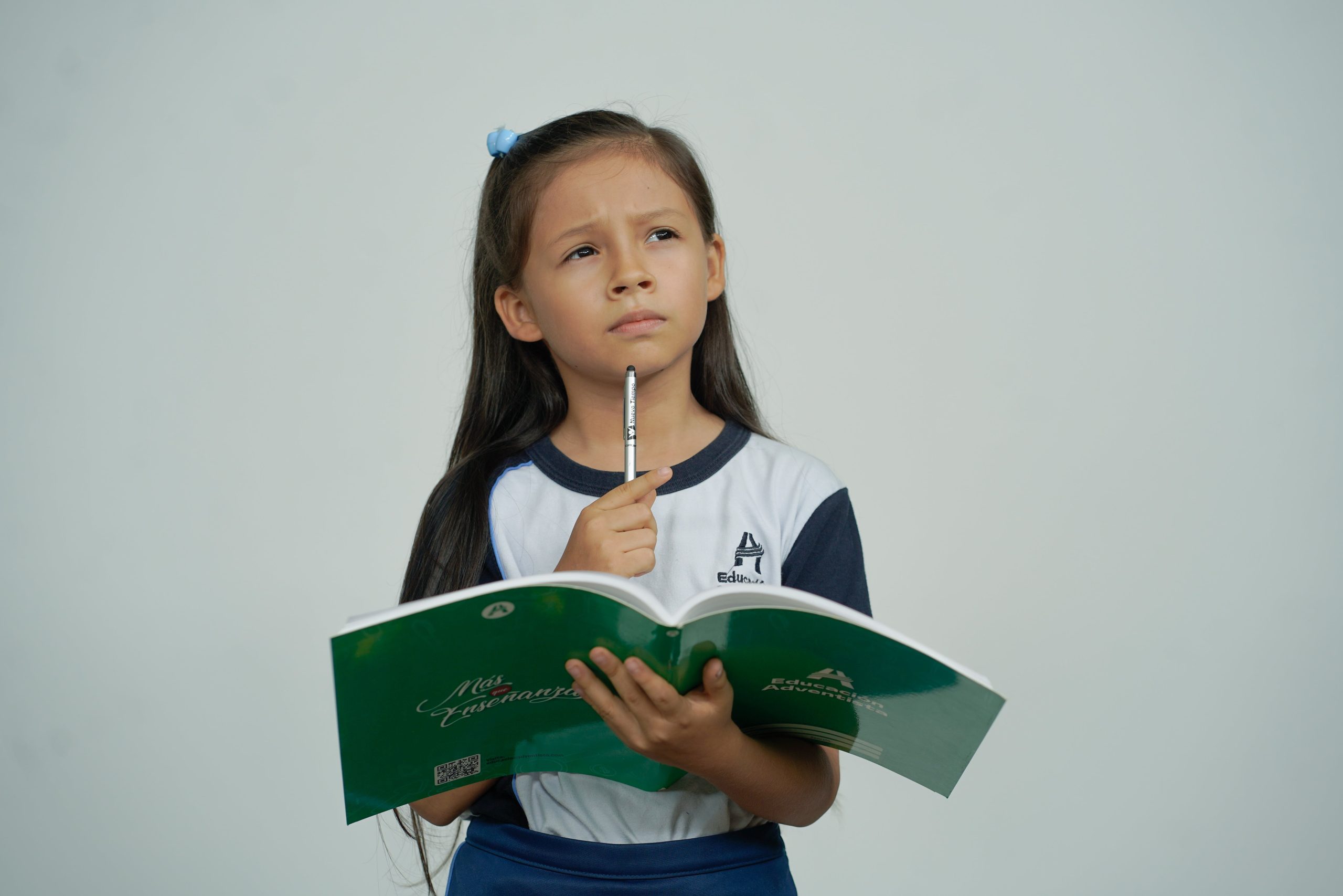 Dziewczynka w wieku szkolnym trzyma podręcznik do nauki języka angielskiego i zastanawia się.